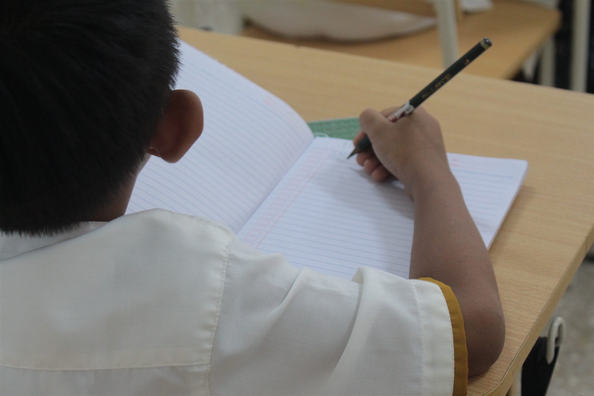 Siswa TSLS menulis dengan teliti di meja belajar